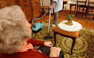 Ældre kvinde sidder i lænestol, mens hjemmeplejen støvsuger